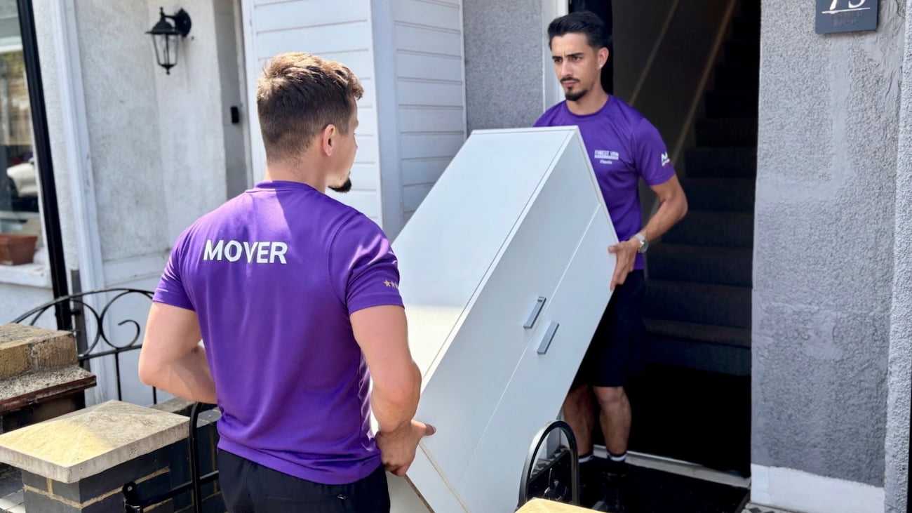 Removal specialists manoeuvring a small cabinet into a London property during a student move