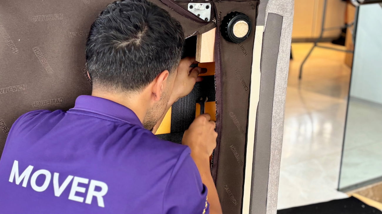 A professional removal specialist using tools to dismantle a sofa arm for a house move.