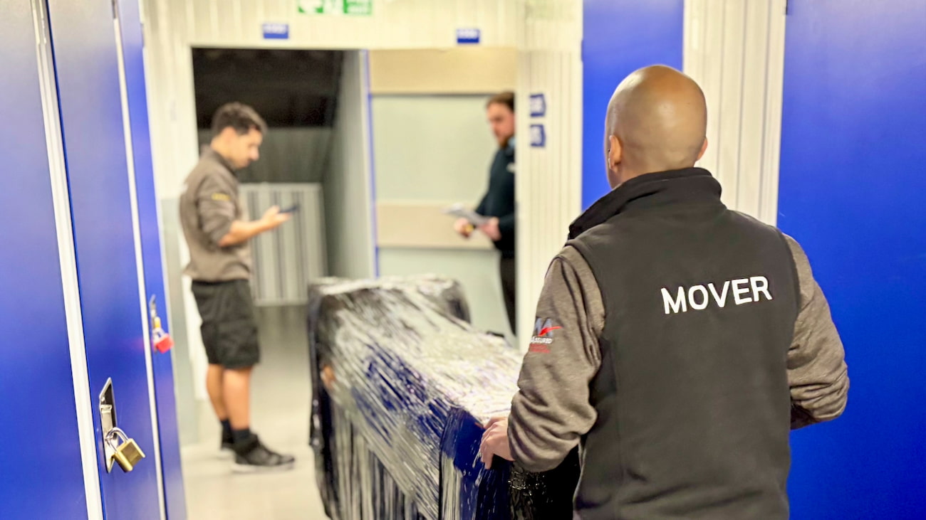 Removal specialists moving a wrapped item of furniture into a storage unit